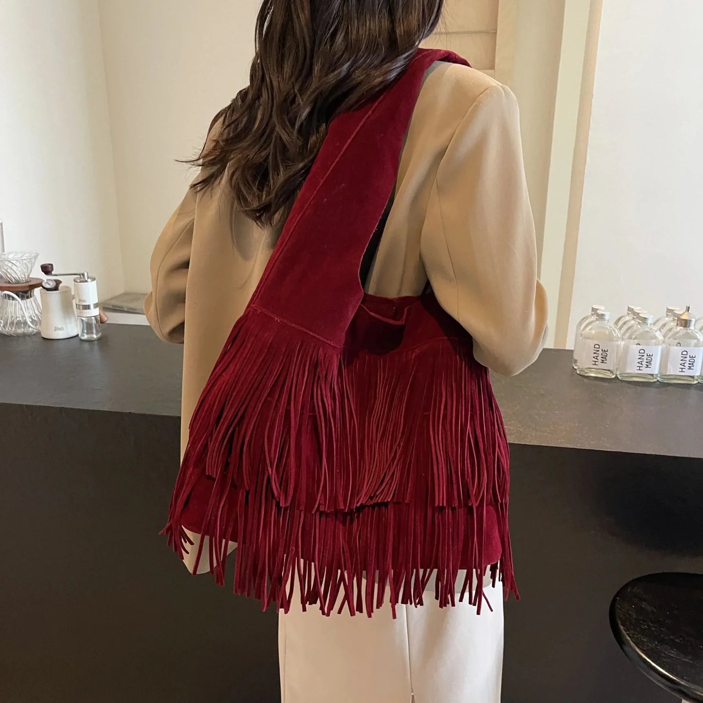 Woman wearing a burgundy velvet tassel shoulder bag with large capacity in a modern room