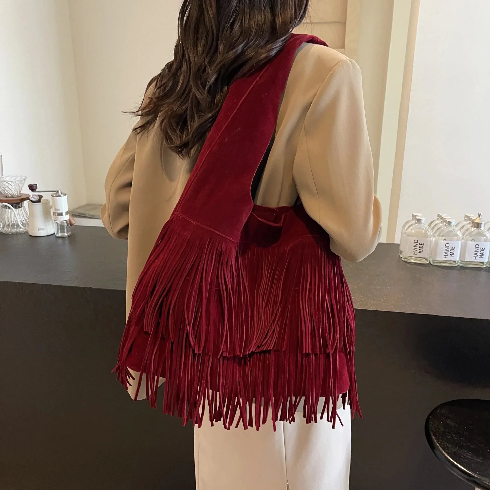 Woman wearing a burgundy velvet tassel shoulder bag with large capacity in a modern room