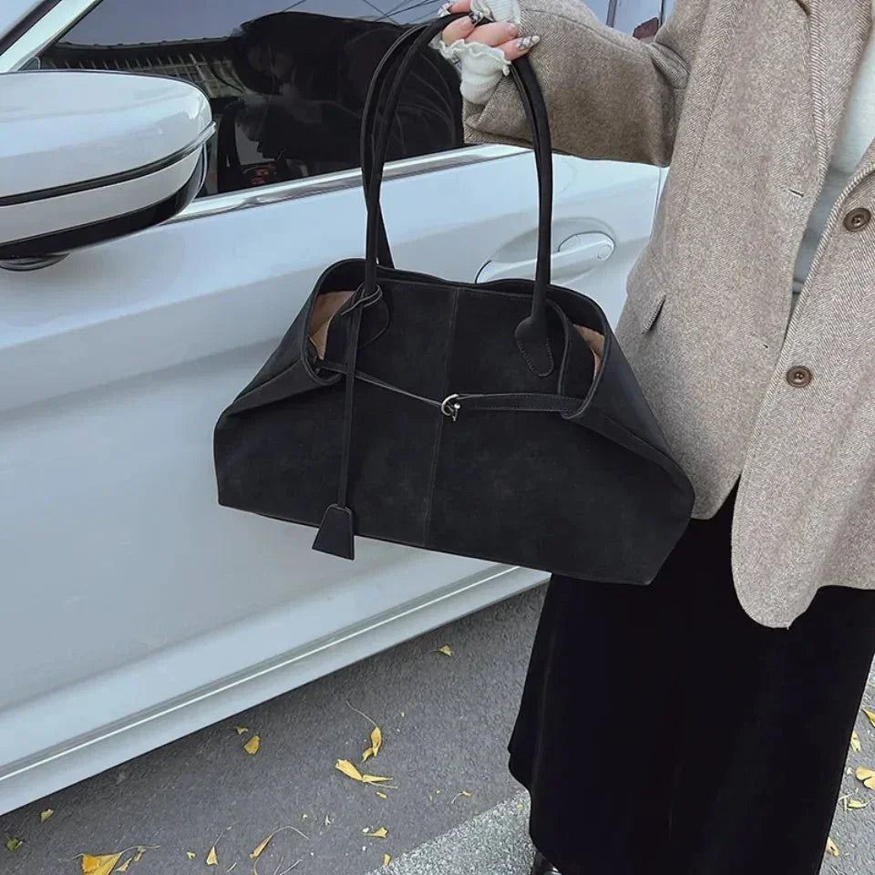 Large black vegan suede handbag with retro design, held by a woman in a coat outdoors