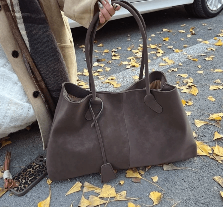 Large dark brown vegan suede handbag for women in retro style, outdoors on autumn leaves
