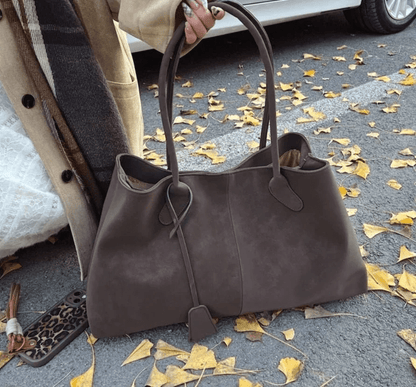 Large dark brown vegan suede handbag for women in retro style, outdoors on autumn leaves