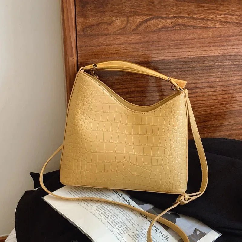 Beige crocodile pattern handbag for women with top handle and crossbody strap on wooden background