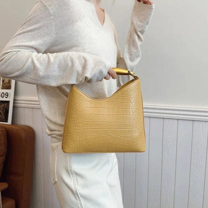 Woman holding yellow crocodile pattern top handle handbag, casual outfit, indoor setting