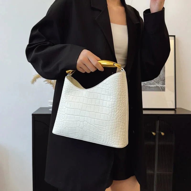Woman holding white crocodile pattern handbag with gold top handle, wearing black blazer