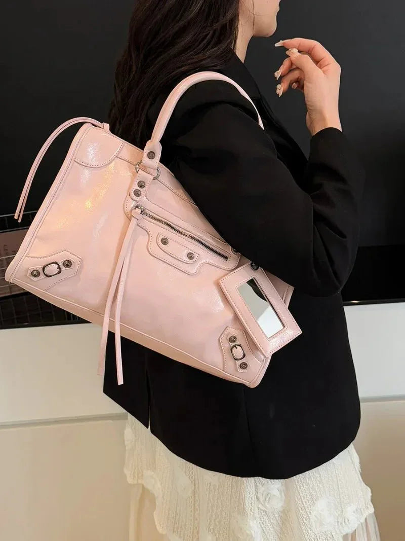 Woman carrying a pastel pink handbag with metal accents and zipper details
