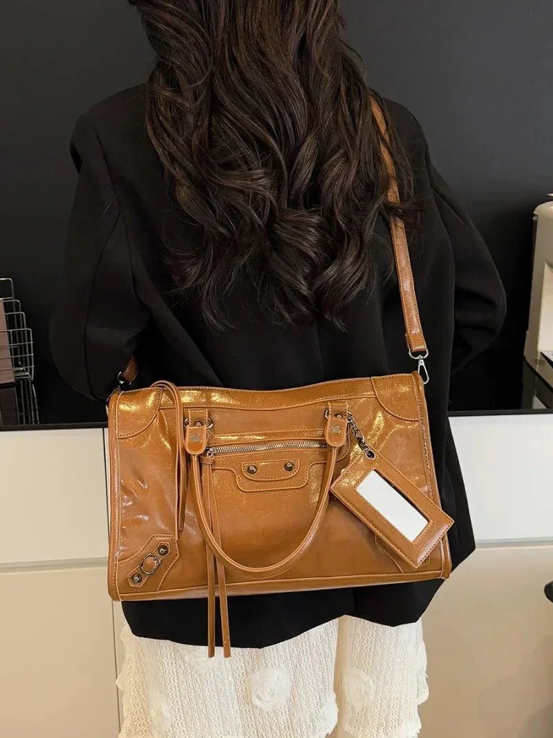 Woman carrying a brown minimalist handbag with a spacious interior and front zipper pocket.