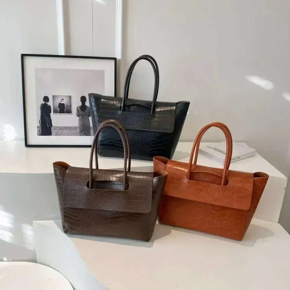 Three stylish crocodile pattern handbags for women in brown, black, and tan on white tables.