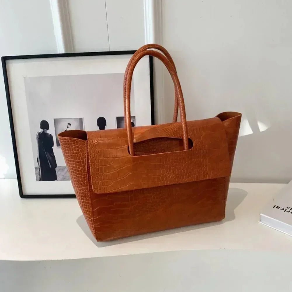 Dark brown crocodile pattern large tote handbag with top handles on a white table