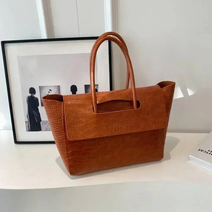 Dark brown crocodile pattern large tote handbag with top handles on a white table