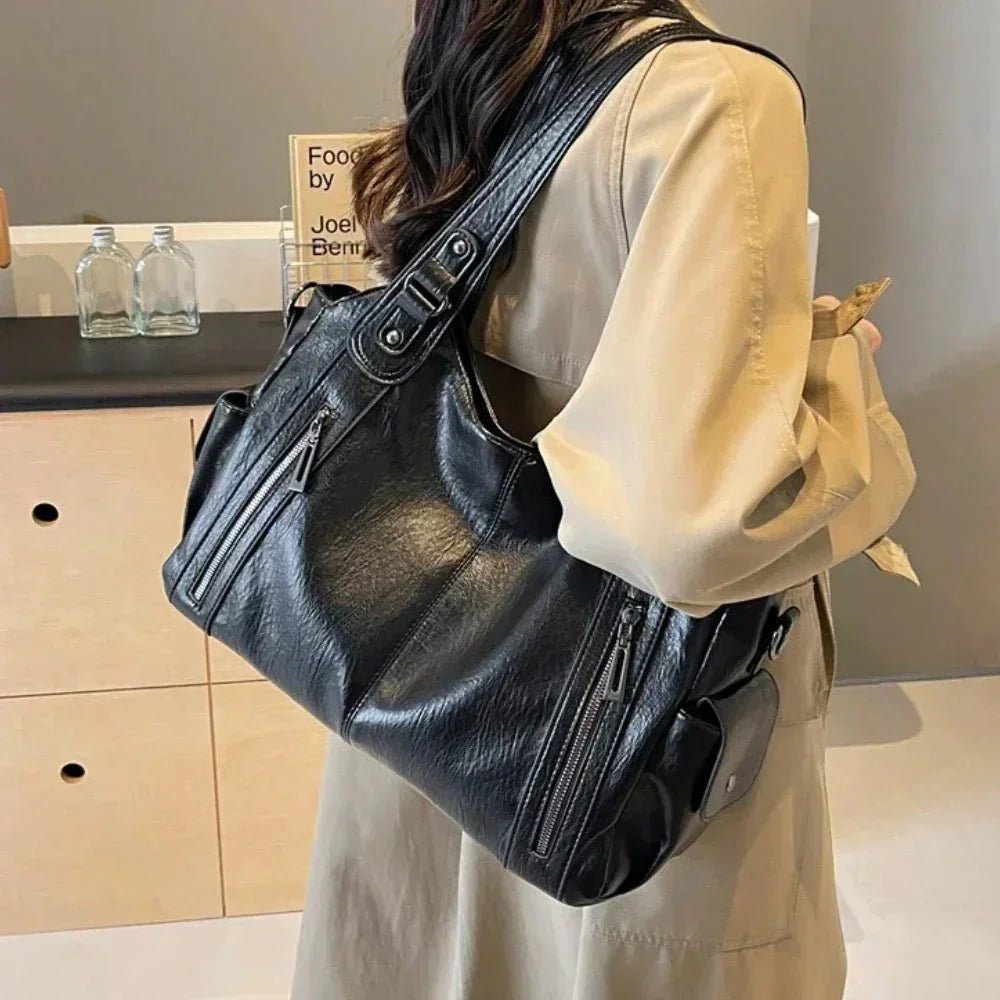 Woman carrying a spacious black leather shoulder bag with zipper pockets indoors.