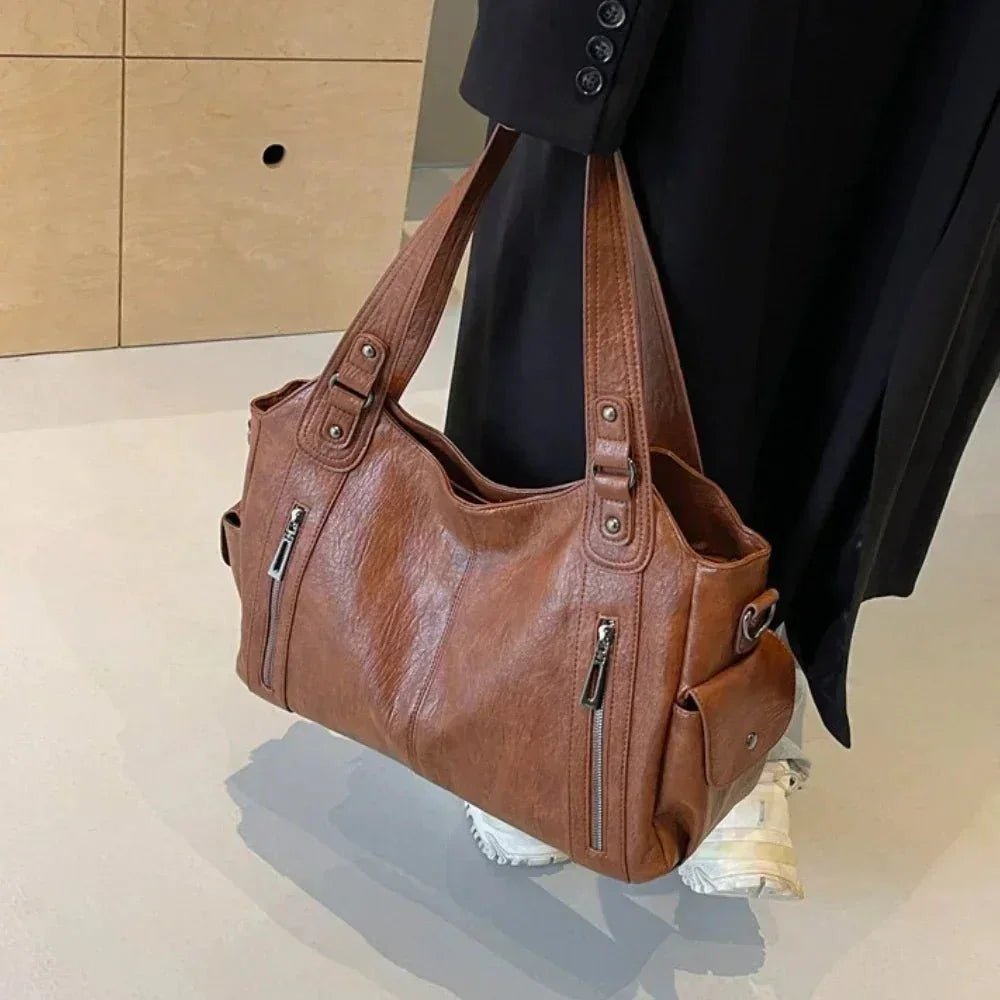 Brown stylish shoulder bag for women with zipper pockets, worn by person in black coat