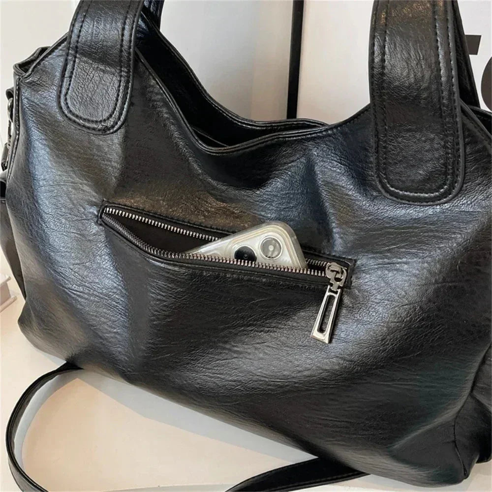 Black shoulder bag for women with spacious zip pocket holding a smartphone