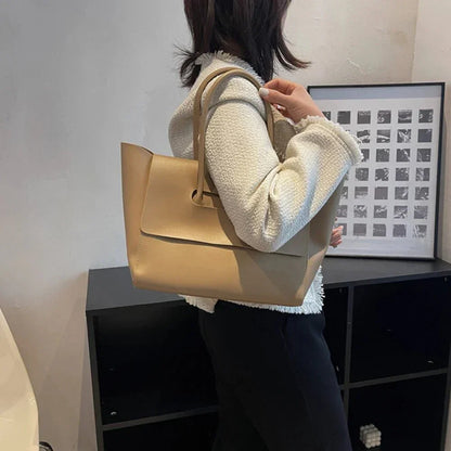 Woman carrying large beige shoulder tote purse with minimalist design indoors