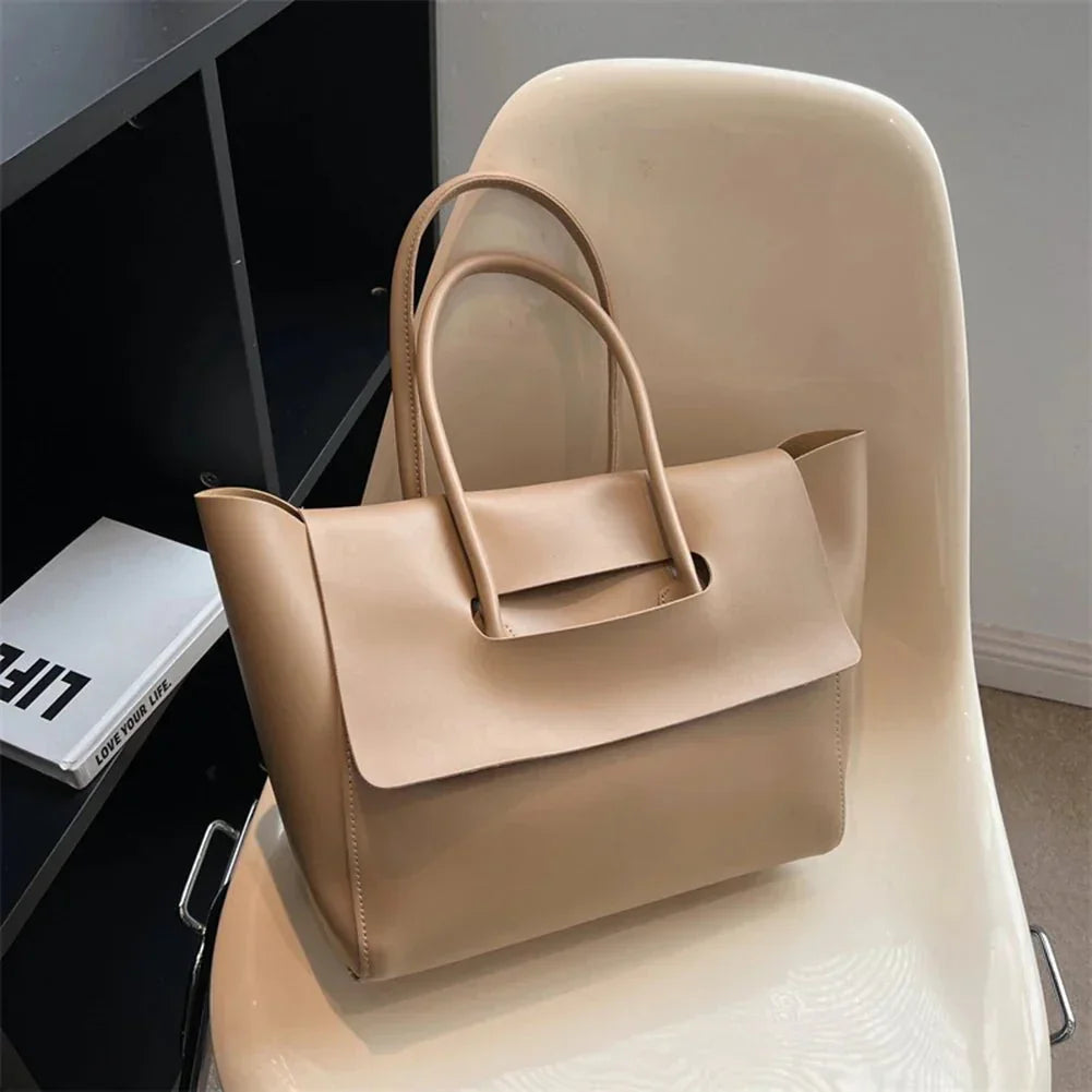 Beige vegan leather tote purse with top handles on a cream chair, large capacity, minimalist design