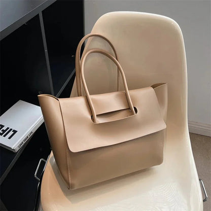 Beige vegan leather tote purse with top handles on a cream chair, large capacity, minimalist design