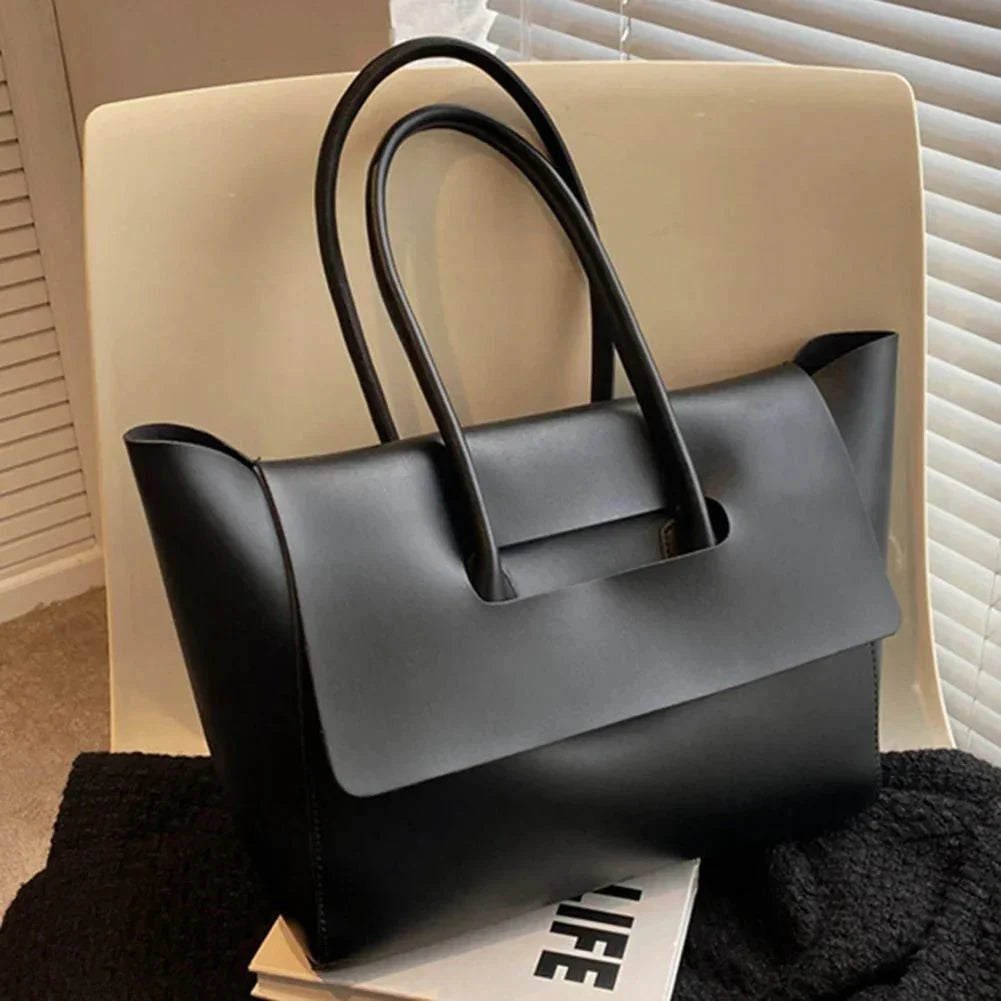 Black vegan leather shoulder tote purse with large capacity and versatile design on chair