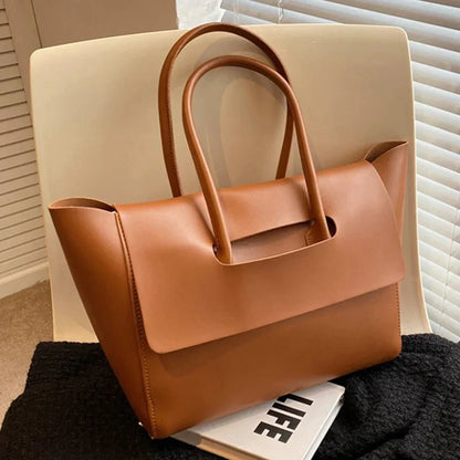 Brown vegan leather tote purse with large capacity and modern flap design on a chair.