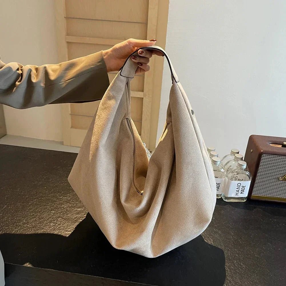 Beige suede hobo handbag with zipper, large capacity, held by hand on a black table