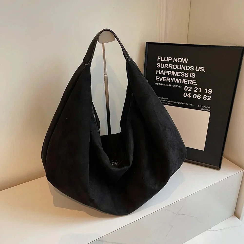 Black suede hobo handbag with zipper, large capacity, displayed on a white shelf.