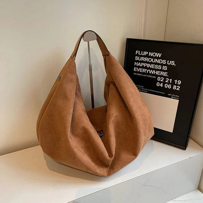 Brown suede hobo handbag with zipper, large capacity, displayed on a white surface indoors.